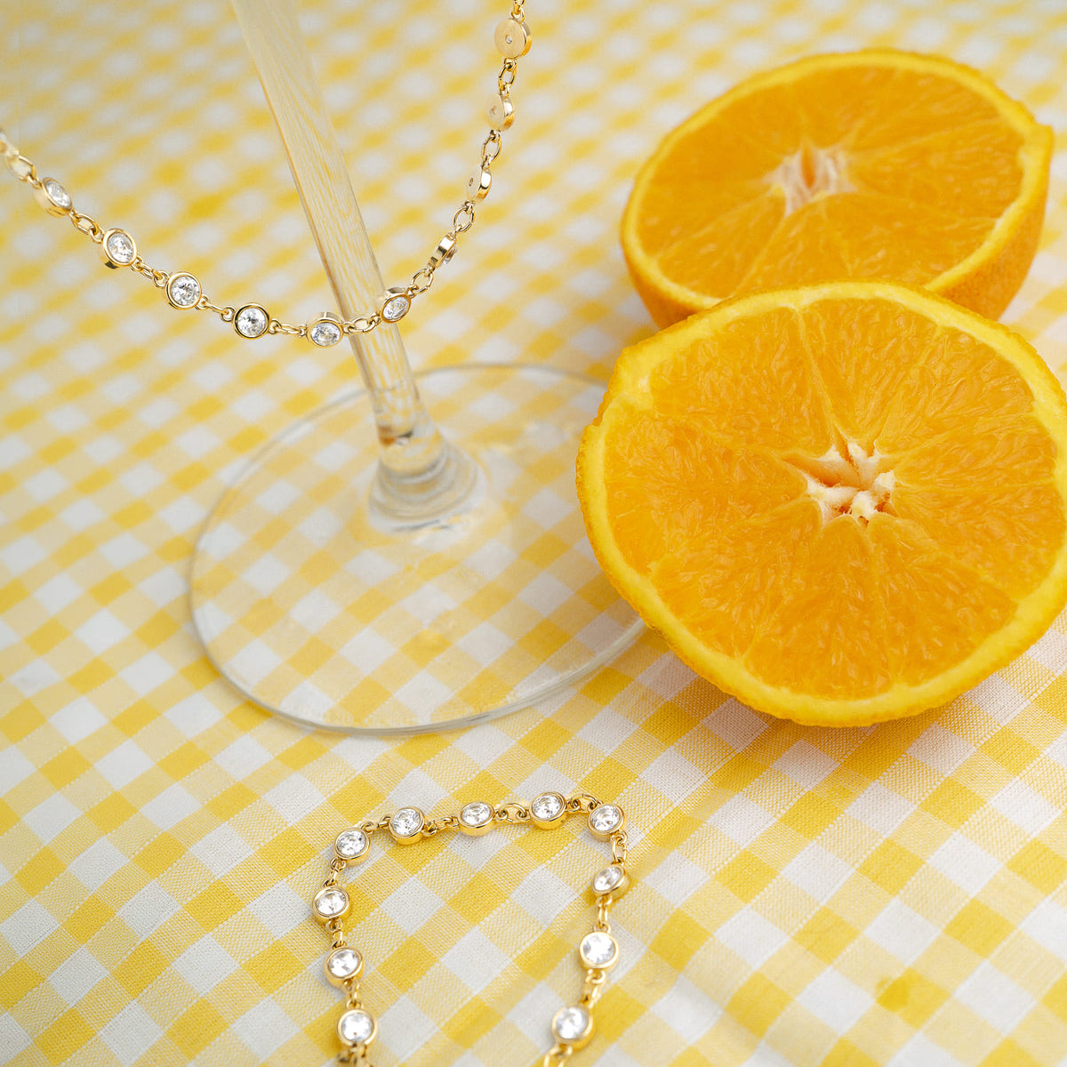 Bijoux dorés sertis de zircons posés sur une nappe vichy jaune avec des oranges