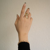 Main portant une bague double cœur et un bracelet dorés