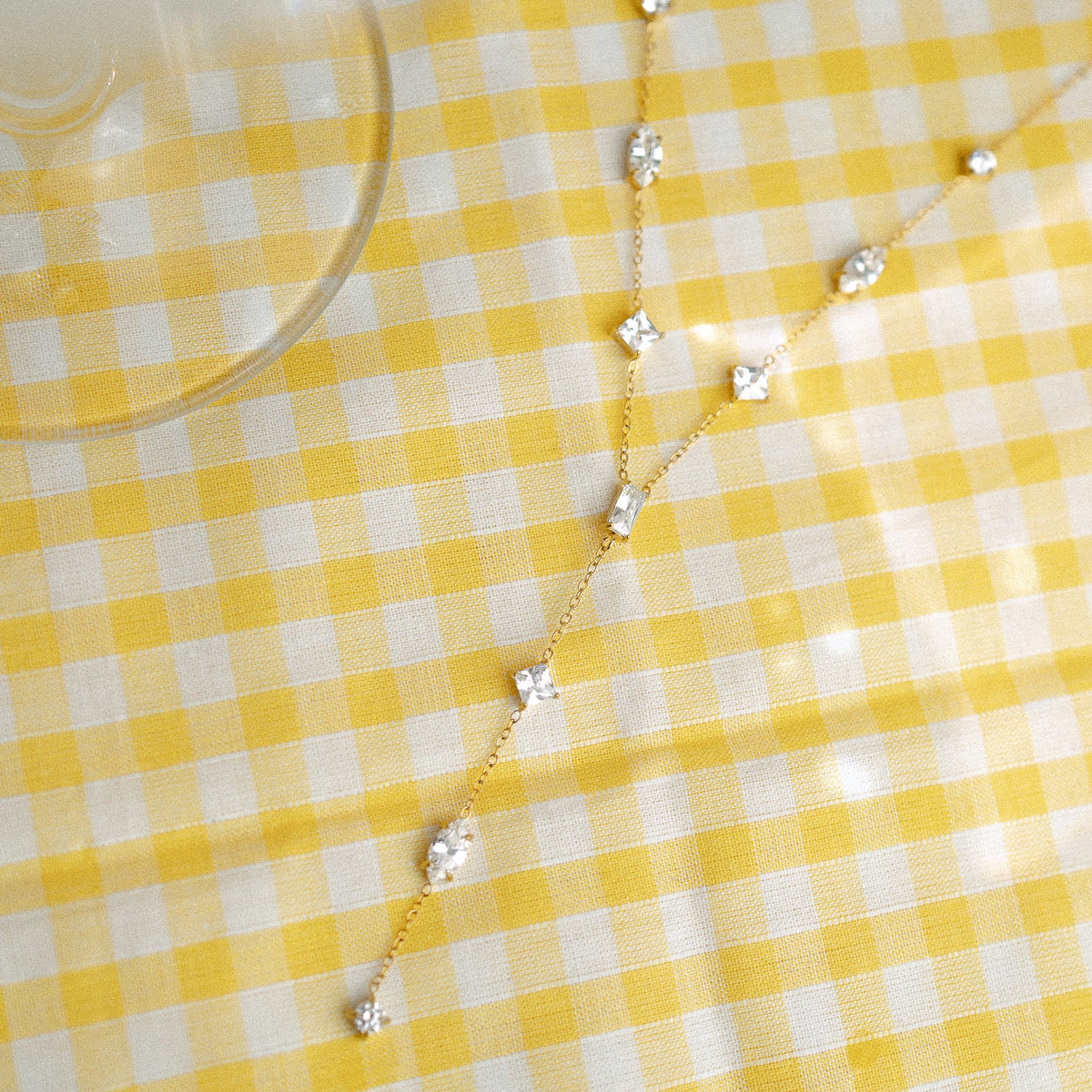 Collier en Y doré serti de zircons posé sur une nappe vichy jaune