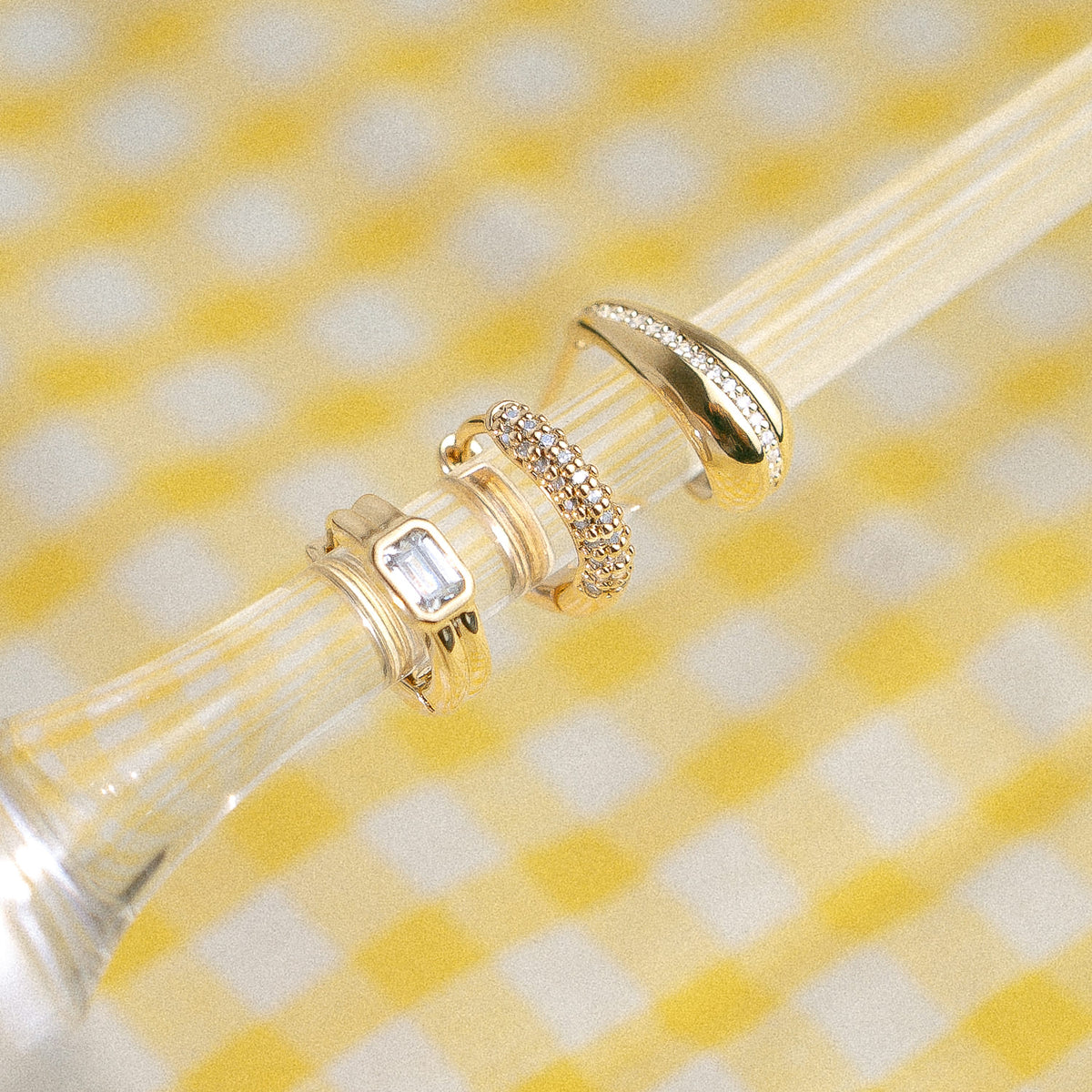 Mini créoles serties dorées posées sur un verre, nappe vichy jaune