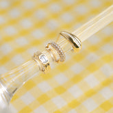 Mini créoles serties dorées posées sur un verre, nappe vichy jaune