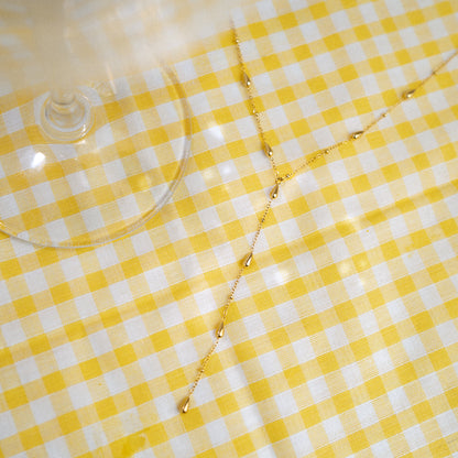Collier en Y doré posé sur une nappe vichy jaune