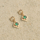 Paire de boucles en plaqué or à losange et zircon vert posées sur le sable