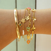 Bracelets dorés à breloques fleurs et perles superposés au poignet