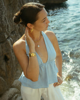 Femme en top bleu portant des colliers dorés au bord de la mer