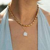 Collier à perles ovales dorées et collier à pendentif nacre portés au cou