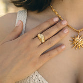 Main portant une bague dôme à godrons et un collier soleil dorés