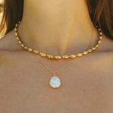 Collier à pendentif nacre porté avec un collier à perles dorées