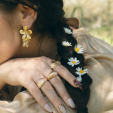 Main portant plusieurs bagues dorées, cheveux ornés de marguerites
