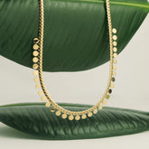 Collier doré à pampilles rondes posé sur une feuille verte