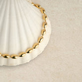 Collier à perles ovales dorées posé sur un coquillage