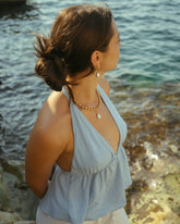 Femme de dos portant des colliers dorés et un pendentif nacre face à la mer